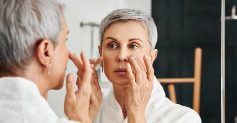 Frau betrachtet ihr Gesicht im Spiegel