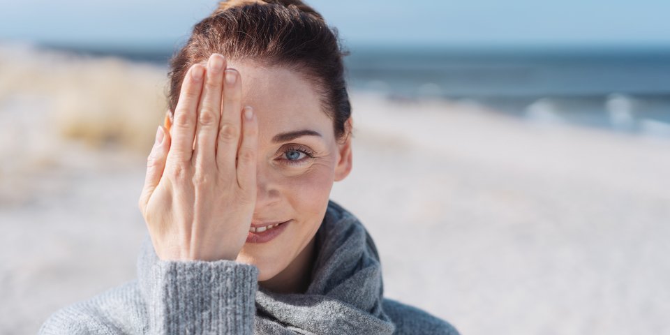 Frau am Meer hält Hand vor ein Auge